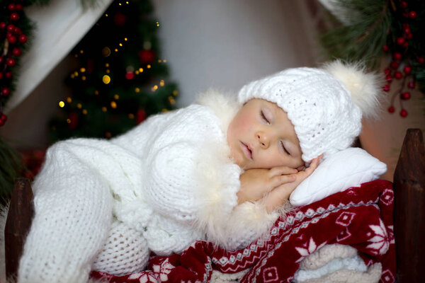 Adorable little toddler baby boy dressed in canta claus costume, sleeping in baby bed in front of teepee decorated for Christmas