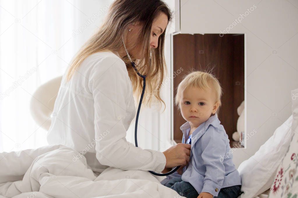 Young doctor, examiing sick baby boy on a home visitation, child lying ill in bed