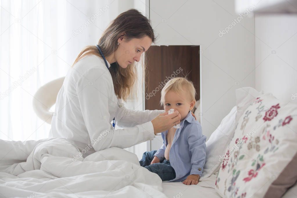 Young doctor, examiing sick baby boy on a home visitation, child lying ill in bed