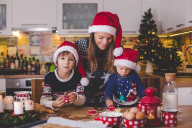 Tatlı çocuk ve ağabeyi, çocuklar, annenize mutfakta Noel kurabiyeleri hazırlarken yardım ediyorlar.