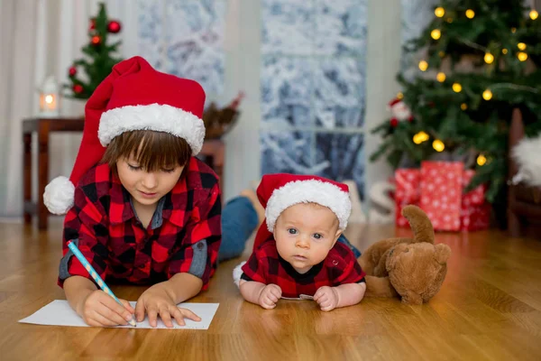 可爱的新生男婴与圣诞帽 躺在地板上 他的哥哥写信给圣诞老人 — 图库照片