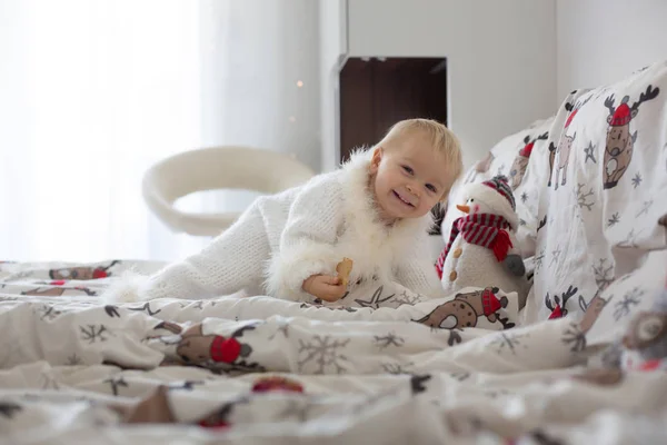 愛らしい赤ちゃんの少年 Handknitted 全体的なクリスマスの日にベッドでクッキーを食べて — ストック写真