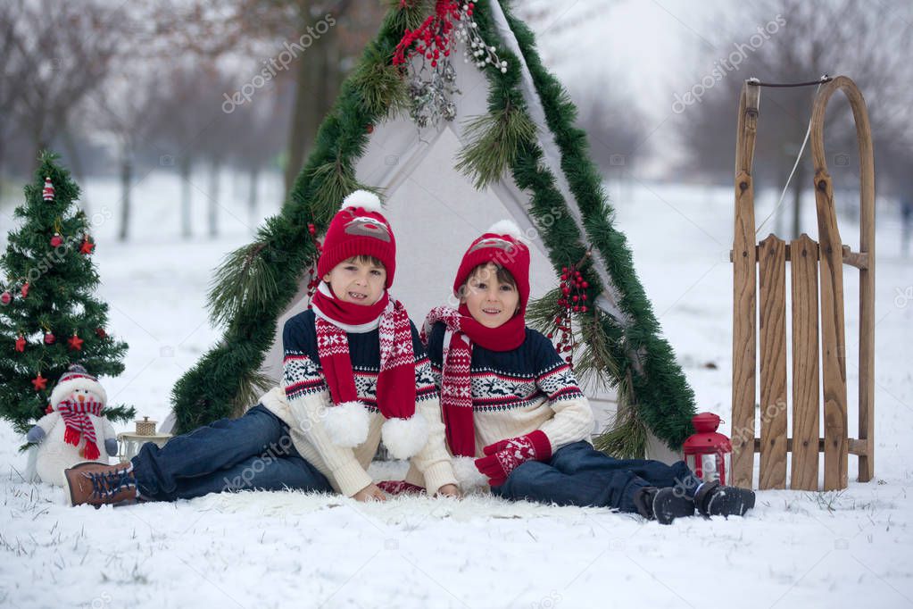 Happy family with kids, having fun outdoor in the snow on Christmas, playing with sledge, teepee and christmas decoration