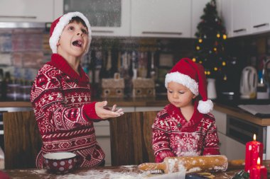 Tatlı çocuk ve ağabeyi, çocuklar, annenize mutfakta Noel kurabiyeleri hazırlarken yardım ediyorlar.