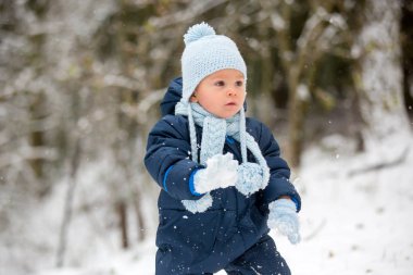 Tatlı küçük çocuk, kış günü dışarıda karla oynuyor, kar yağıyor.