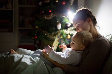 Genç güzel annem, emzirme gece, onun yeni doğan bebek çocuk loş ışık. Noel anne emzirme yürümeye başlayan çocuk