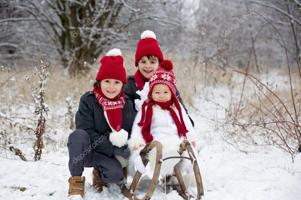 Cute little toddler boy and his older brothers, playing outdoors with snow on a winter day, snowing