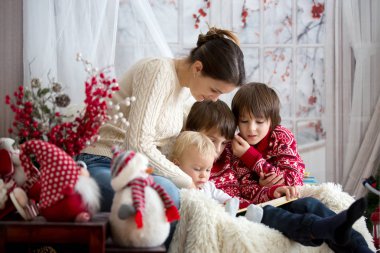 Anne oğulları bir karlı kış gününde, kışın rahat koltukta oturan çocuklar için kitap okur