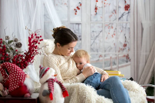 Anne, bebeğini emziriyor rahat koltukta oturuyor, kış vakti kar yağıyor.