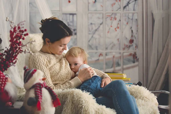 Anne, bebeğini emziriyor rahat koltukta oturuyor, kış vakti kar yağıyor.