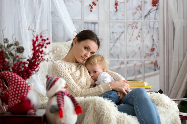 Anne, bebeğini emziriyor rahat koltukta oturuyor, kış vakti kar yağıyor.