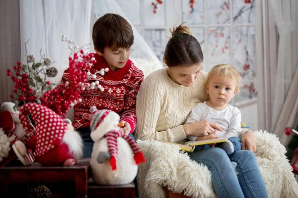Anne oğulları bir karlı kış gününde, kışın rahat koltukta oturan çocuklar için kitap okur