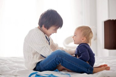 Küçük yürümeye başlayan çocuk, küçük kardeşi için güneşli yatak odasında evde Doktor ile oynarken