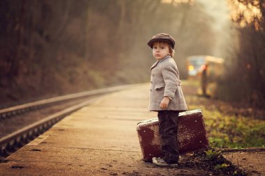 Adorable boy on a railway station, waiting for the train with suitcase and teddy bear, vintage look clipart