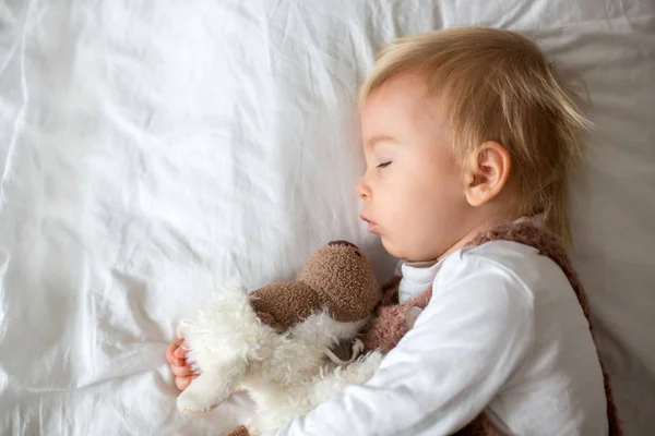 可爱的男婴在可爱的整体 睡在床上与泰迪熊填充玩具 冬天风景在他身后 — 图库照片