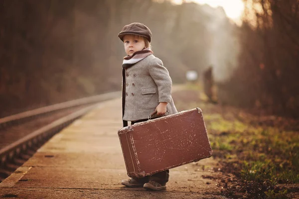 可爱的男孩在火车站 等待火车与手提箱和泰迪熊 复古的样子 — 图库照片