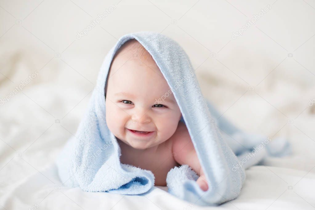 Cute little baby boy, relaxing in bed after bath, smiling happily, daytime