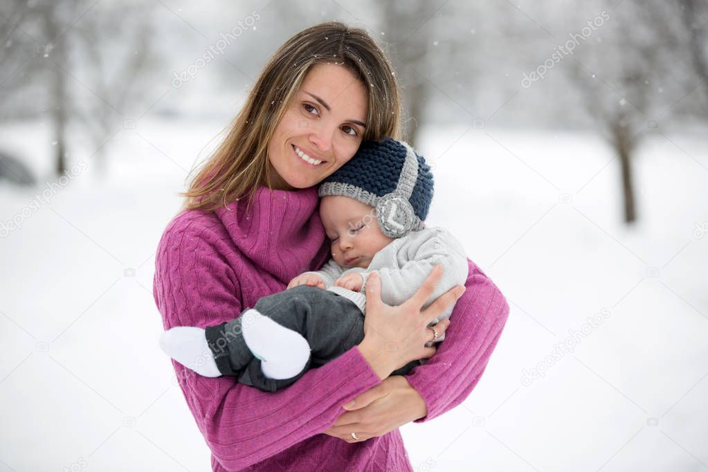 Beautiful mother and cute baby boy in knitted sweater, having taken their beautiful winter outdoor portrait on a sunny winter snowy day