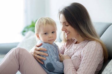 Onu evde, sarılma onun hasta yürümeye başlayan çocuk tutan genç anne, güneşli oturma odası