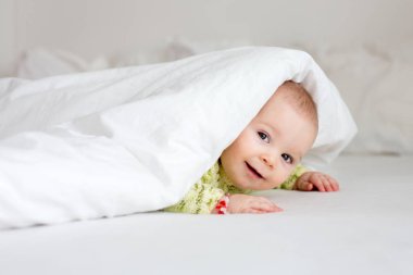 Mutlu bir şekilde gülümseyerek evde yatak yatak, yorgan altında oynayan sevimli küçük altı aylık oğlu,