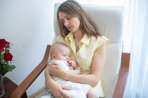 居心地の良い日当たりの良いベッドルームの肘掛け椅子に座っている若い母彼女の赤ん坊を保持している スリープ状態に彼を揺動 — ストック写真