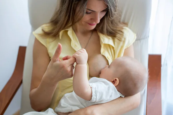 居心地の良い日当たりの良いベッドルームの肘掛け椅子に座っている彼女の男の子の Brestfeeding を保持している若い母親 — ストック写真
