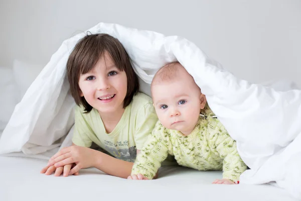 かわいい ヶ月歳の赤ちゃん男の子と彼の兄 自宅の寝室のベッドの布団の下で遊ぶ幸せそうに笑って — ストック写真