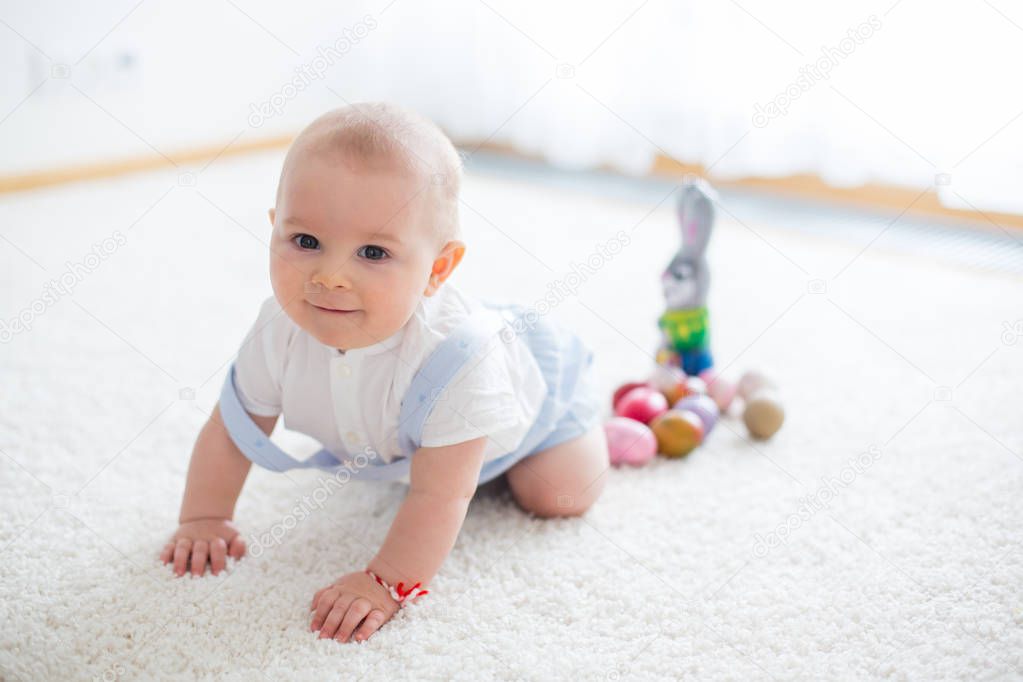 Cute little toddler child, baby boy, in sunny living room playing with  Easter chocolate bunny and colorful Easter eggs