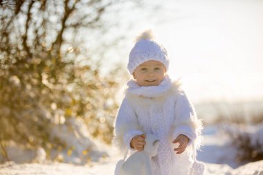 Bebek kışın karda Teddy ile oynuyor. El yapımı beyaz kar elbisesi içinde küçük bir çocuk, gün batımında oyuncak ayıyı tutuyor, kış parkında açık havada oynuyor. Çocuklar karlı parkta oynuyor.