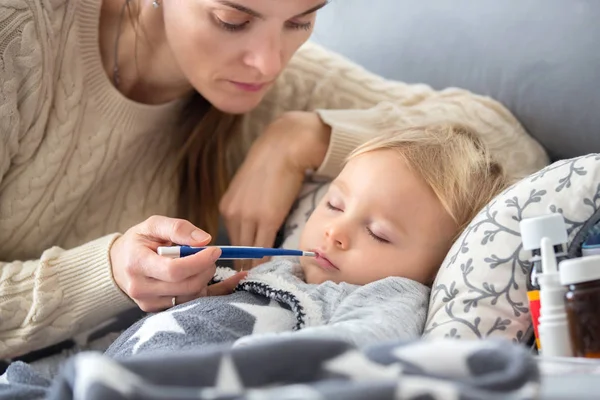 熱のある部屋のソファの上に寝そべってる子供は病気で母親は体温をチェックして家で休んでる — ストック写真