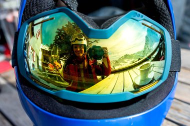 Reflections of woman and children and beautiful mountains on a ski goggles, glass of wine, coffee and cake clipart