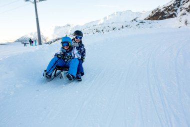 Mutlu insanlar, çocuklar ve yetişkinler, güneşli bir günde Tyrol dağlarda kayar. Çocuklar eğleniyor sledging süre