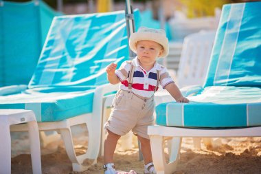 Peluş rahatlatıcı oyuncak ve şapka şemsiye altında sahilde oynarken şık küçük bebeğim