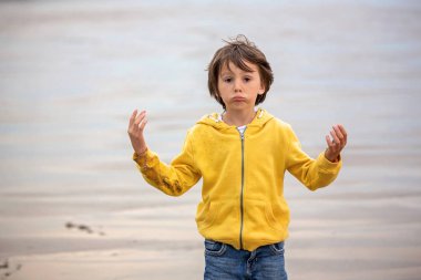 Sevimli güzel çocuk, kum ile sahilde oynarken ve günbatımı, Devon, İngiltere'de suda çalışan çocuk