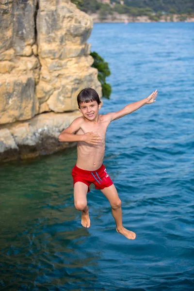 Chico saltando al lago. Niño saltando de un acantilado en el mar . — Foto de Stock