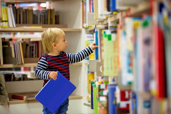 Slimme todller jongen, opleidend in een bibliotheek, het lezen van boeken — Stockfoto