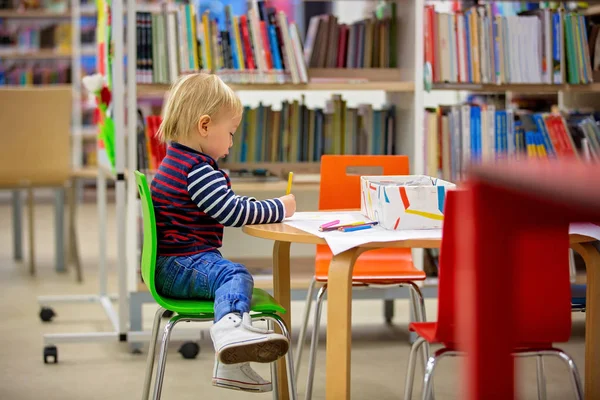 Rapaz esperto, educando-se numa biblioteca, lendo livros — Fotografia de Stock