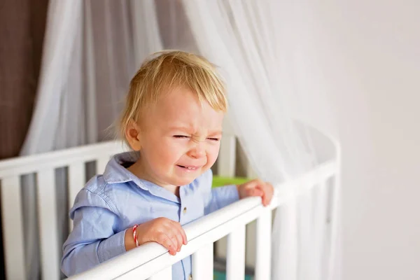 Portrait of bored baby standing in crib. Baby boy stand alone in — Stock Photo, Image