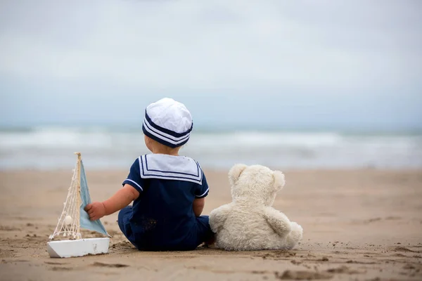 Niño sentado en la playa cerca del agua y juega con un a —  Fotos de Stock