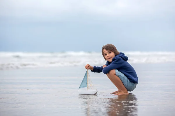 Niño juega con arena en la playa. Lindo niño preescolar con barco de juguete —  Fotos de Stock