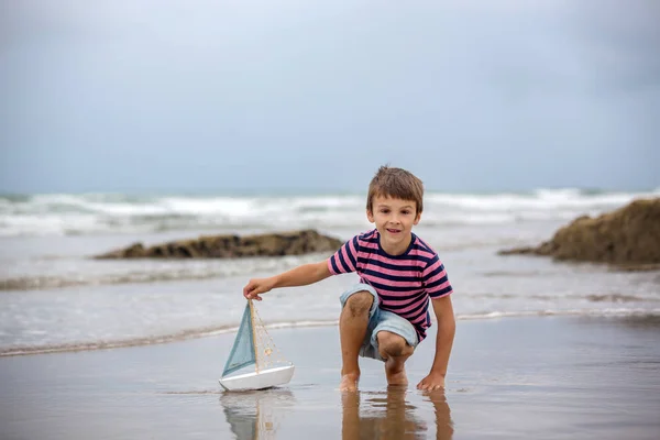 Bambino gioca con la sabbia sulla spiaggia. carino prescolastico ragazzo con giocattolo nave — Foto Stock