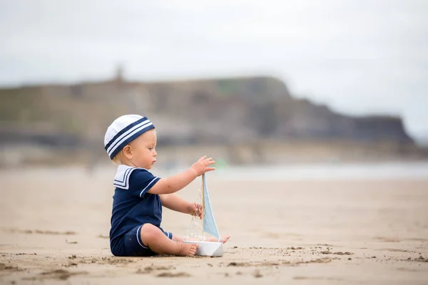 Baby boy sitting on the beach near the water and plays with a to — Stock Photo, Image