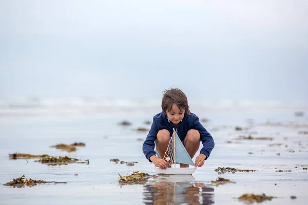Niño juega con arena en la playa. Lindo niño preescolar con barco de juguete — Foto de Stock