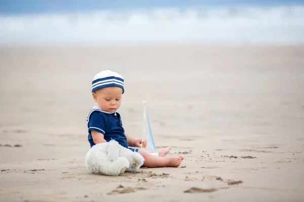 Bambino seduto sulla spiaggia vicino all'acqua e gioca con un a — Foto Stock