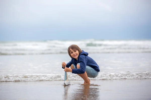 Niño juega con arena en la playa. Lindo niño preescolar con barco de juguete — Foto de Stock