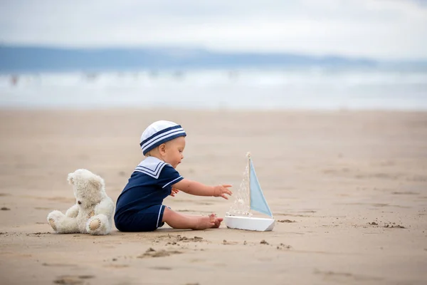 Niño sentado en la playa cerca del agua y juega con un a —  Fotos de Stock