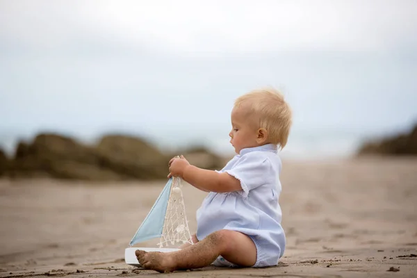 Niño sentado en la playa cerca del agua y juega con un a —  Fotos de Stock