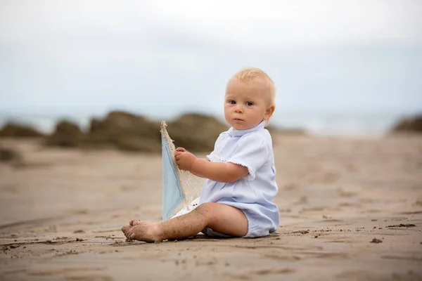 Bambino seduto sulla spiaggia vicino all'acqua e gioca con un a — Foto Stock