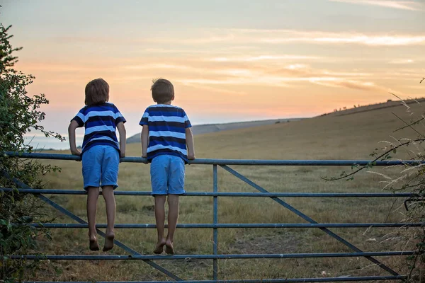 İki çocuk, okyanus üzerinde gün batımı manzarası eşliğinde, ayakta — Stok fotoğraf