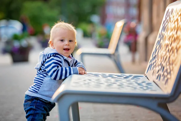 Roztomilý chlapeček, stojící vedle lavičky v krásném městě — Stock fotografie